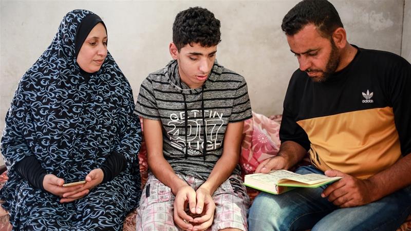 Saleh Ashour, 16, who was blinded by an Israeli bullet last year, sits between his parents at their home in the Gaza Strip [Hosam Salem/Al Jazeera]